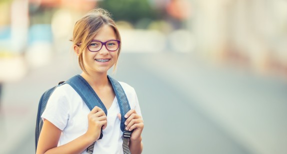 Schülerin mit Zanspange grinst vor unscharfem Hintergrund